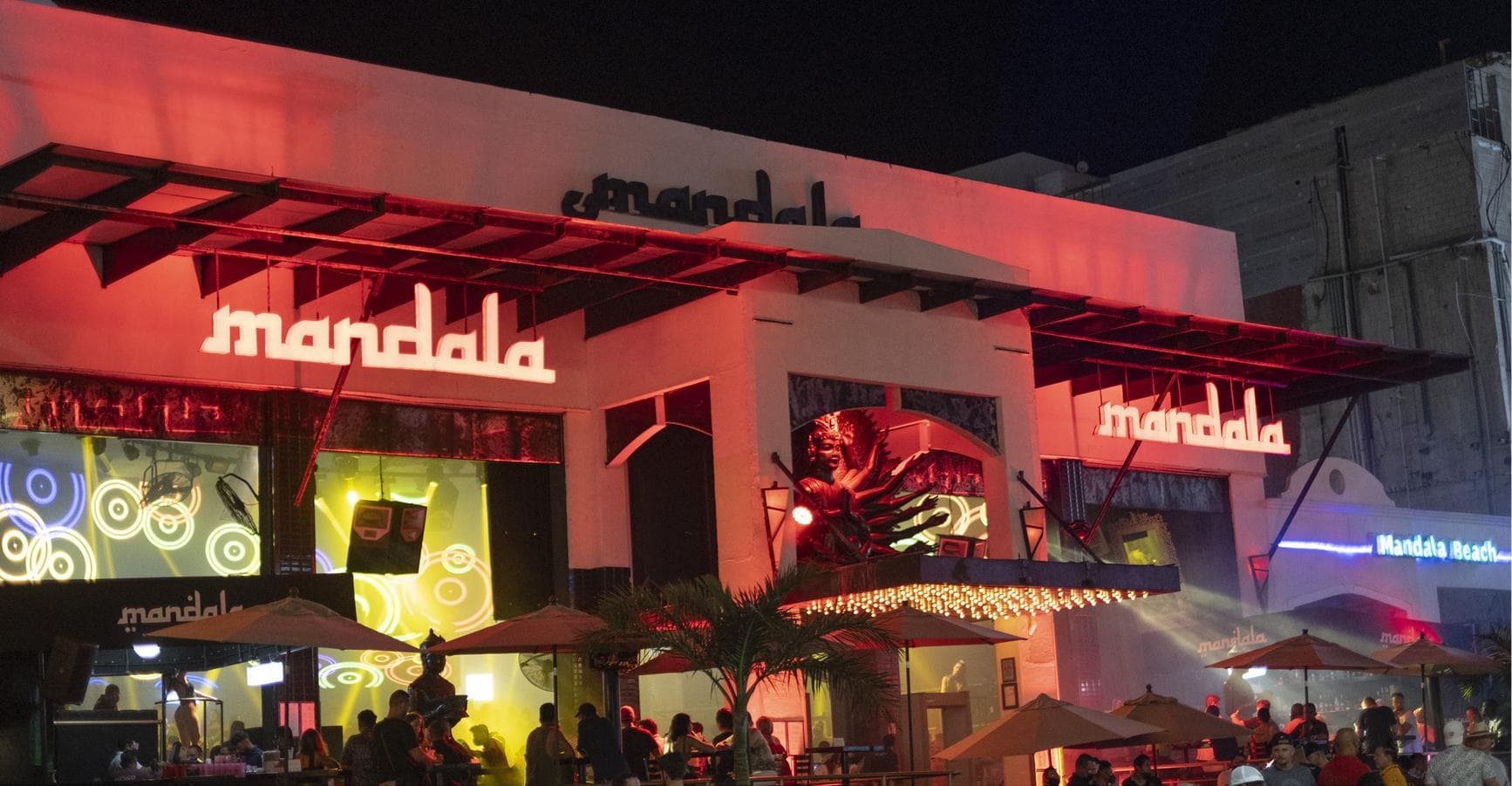 The club's façade at night, its neon sign and the terrace open to the boulevard.