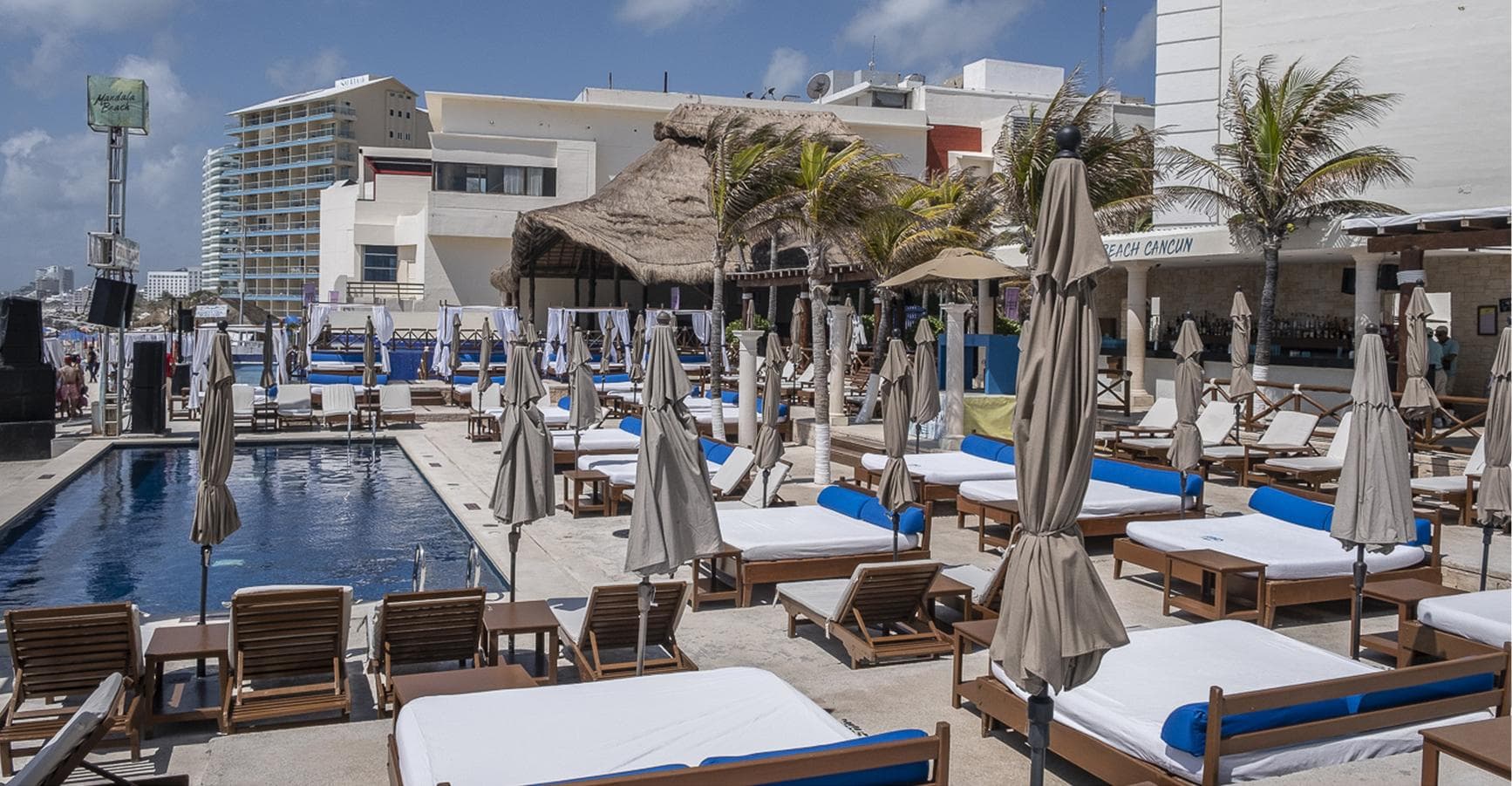 The beach club's pool at midday, with loungers and closed parasols facing the sea.